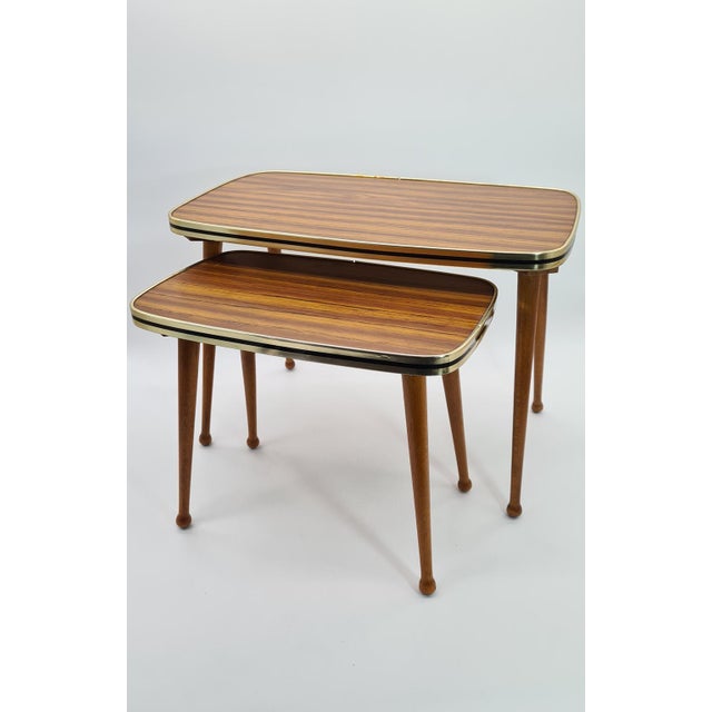 A set of retro-style nesting tables, popular in the 1960s and 1970s. They feature laminate (Formica) tops with a teak wood...
