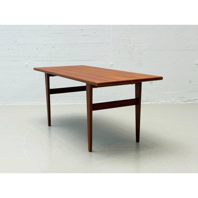 A simple coffee table in the style of the 1970s with clean lines and a warm wood look. The rectangular tabletop features a...