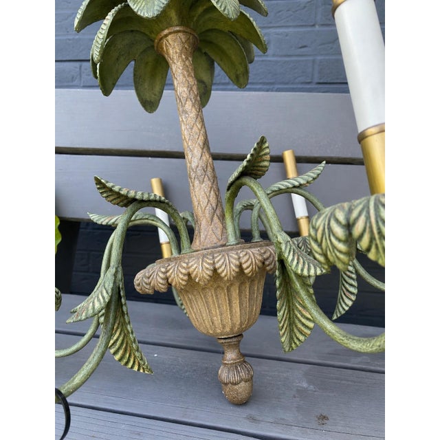 a vintage Hollywood Regency-style tole palm tree chandelier featuring hand-painted metal fronds, a central palm trunk, and...