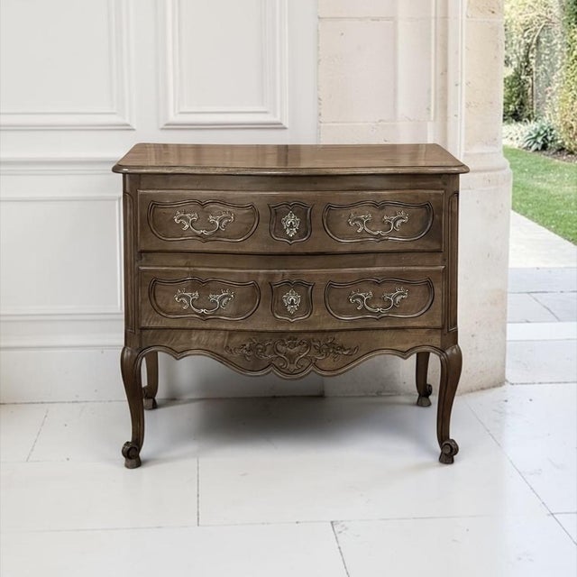 An antique Country French Regence commode handcrafted from French walnut, its warm, mellow patina glowing across a gently...