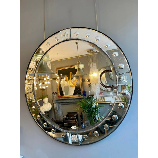 A circular mirror with panelled mirror border in lightly distressed plate, mounted on timber which has an ebonised steel...