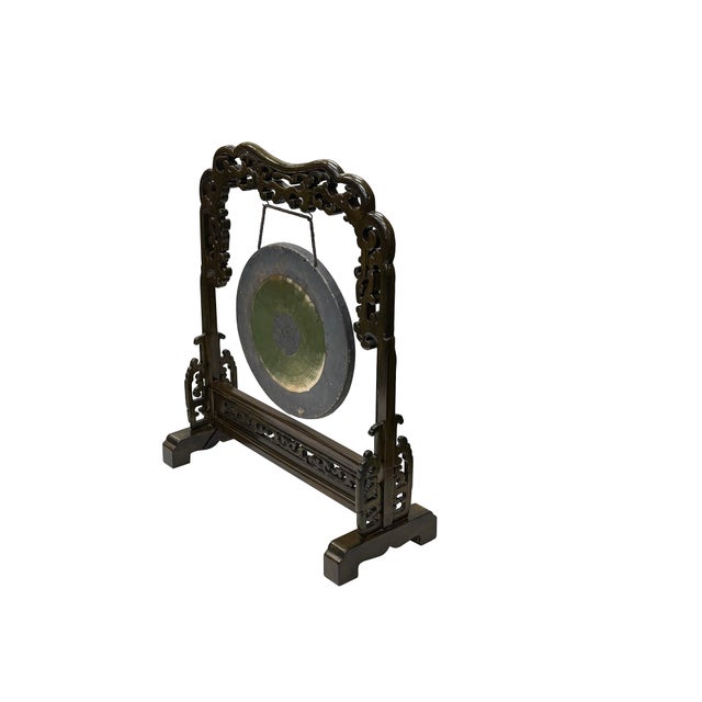 An ornate, dark wood frame stands with elegant poise, cradling a traditional brass gong that serves as its centerpiece....