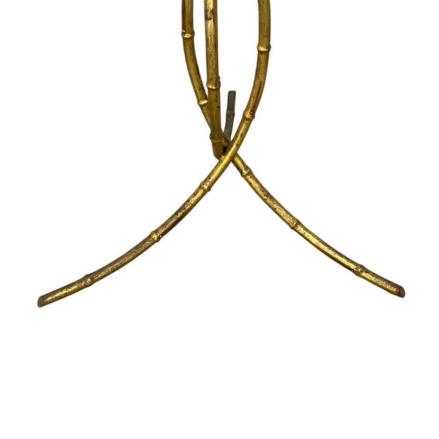 A gilt metal pedestal table featuring a sculptural faux bamboo frame with a round glass top and gracefully curved tripod...