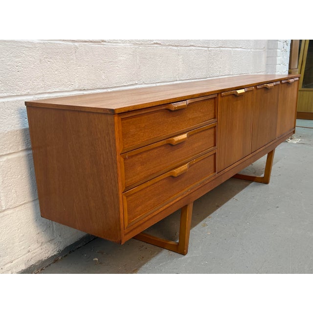 This vintage Mid-Century Modern sideboard was manufactured by Stonehill Furniture in England and features distinctive sled...