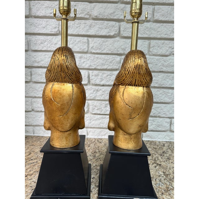 A striking pair of mid century Buddha head table lamps in the highly sought-after Hollywood Regency style of James Mont,...