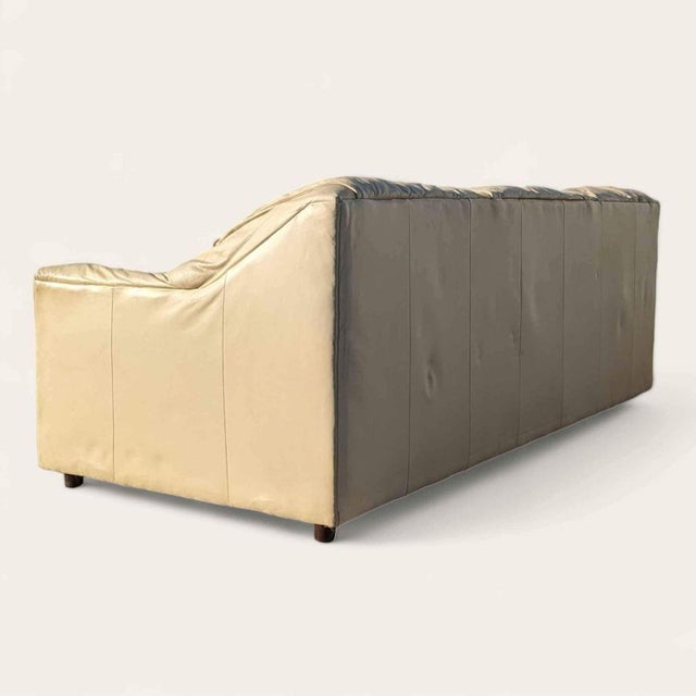 A vintage 1980s postmodern sofa upholstered in supple beige leather. Its broad arms, generous seat, and sculptural profile...