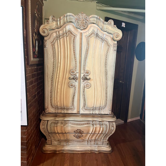 Ornate French-inspired armoire with a Rococo aesthetic, featuring a serpentine silhouette, deep relief carvings, and a...