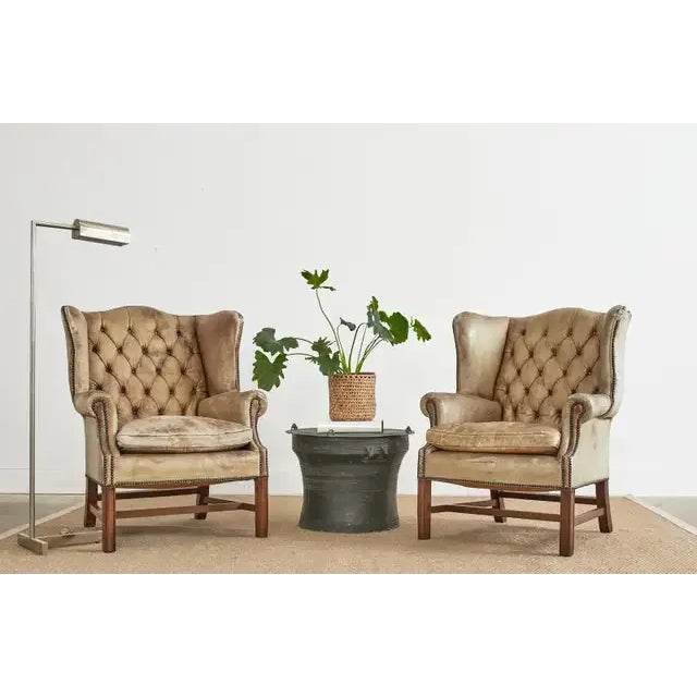 Distressed pair of 19th century English Georgian wingback library chairs. The distinctive pair of armchairs feature a...