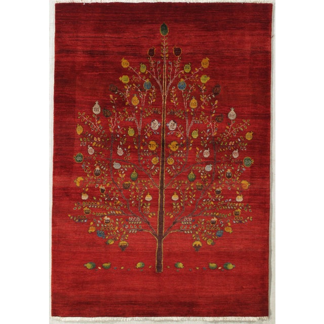 Hand-knotted Persian Gabbeh rug featuring a vibrant red field centered by a detailed tree of life motif adorned with...