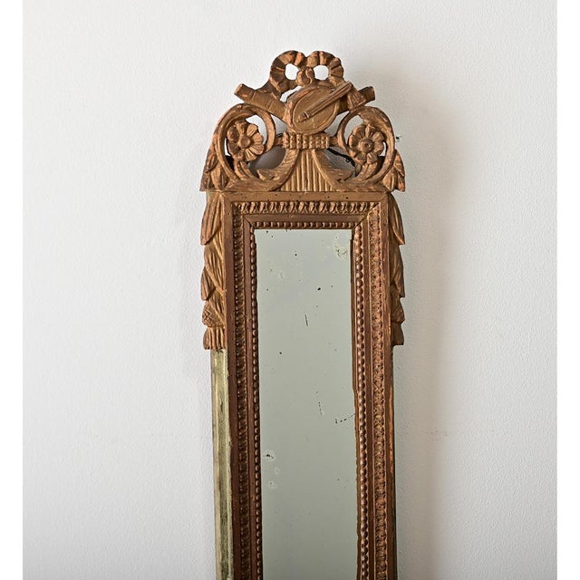 A petite, giltwood mirror from France, late 18th century. Topping the slender piece is carved ornamentation of a dainty...