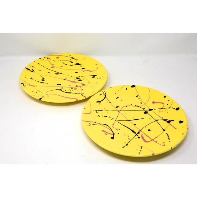 A pair of vintage, handmade 10-inch ceramic dinner plates, decorated with a yellow glaze under black and pink splatter...