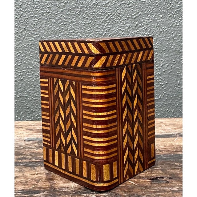 A vintage geometric inlaid wood box characterized by its striking marquetry design. The piece showcases a harmonious blend...
