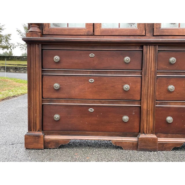 A vintage Georgian style two-piece mahogany china cabinet By Broyhill with a substantial molded crown, four bubble glass-...