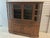 A finely crafted solid wood butler’s pantry or haberdashery with tinted and beveled glass doors on top, three middle...