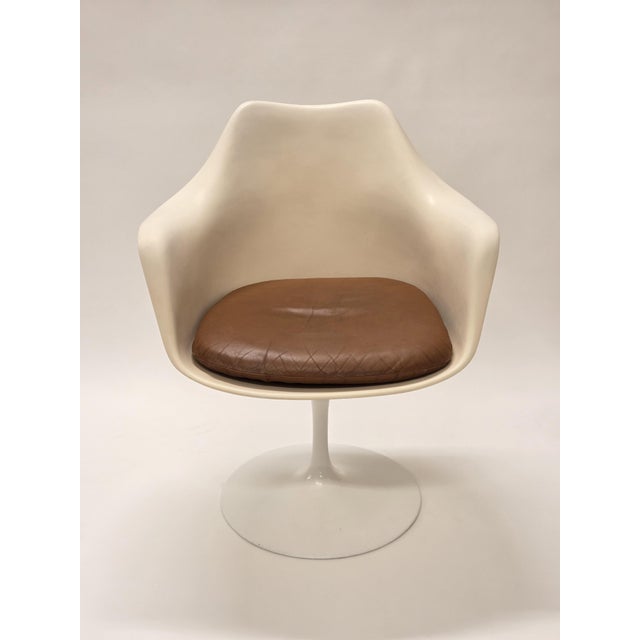 Tulip chair with armrests, white with brown leather upholstered seat cushion. Designer Eero Saarinen. Manufacturer Knoll....