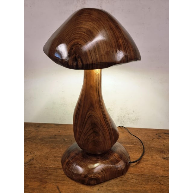 This sculptural table lamp is hand-carved from a single solid piece of hardwood, likely walnut or acacia, and shaped into...