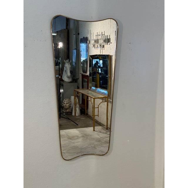 Featuring a softly contoured free-form silhouette, the mirror is framed with a slender brass border that emphasizes its...