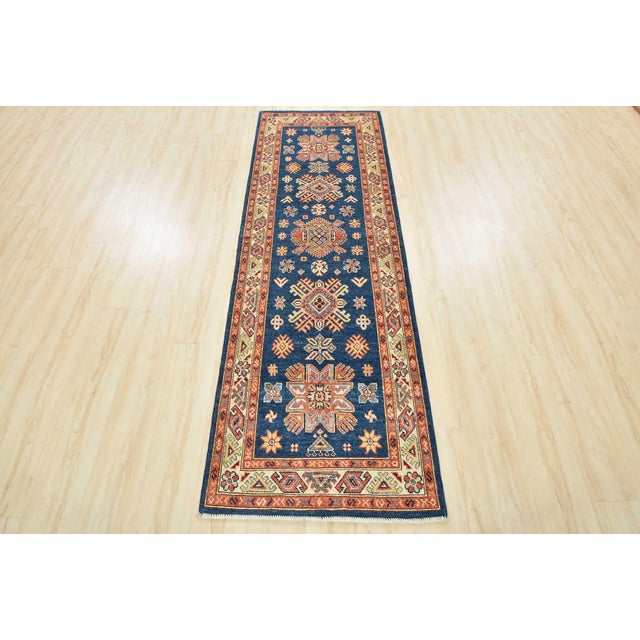 A tribal Kazak runner hand-knotted with an all-wool pile on a cotton foundation. This oriental rug features a row of...