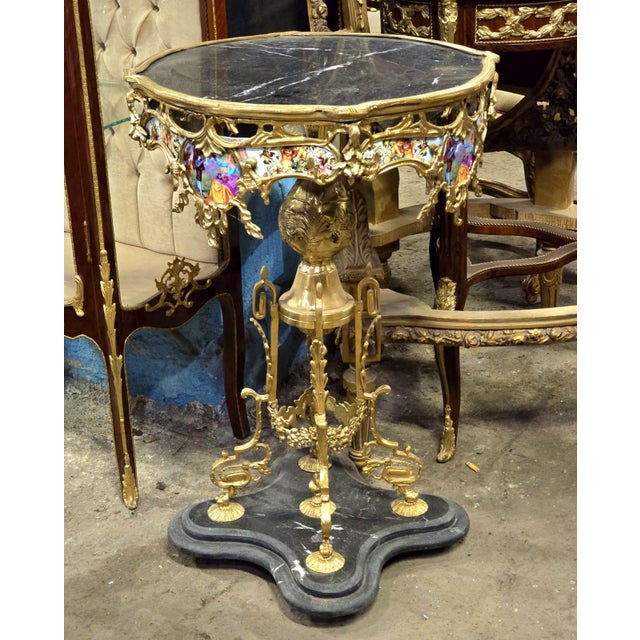 An exquisite French Rococo accent table featuring a luxurious black marble top, elaborate gilded bronze framework, and...