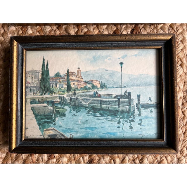 A pair of framed vintage Italian postcards depicting watercolor, waterside scenes. Wood frames have painted gold detailing.