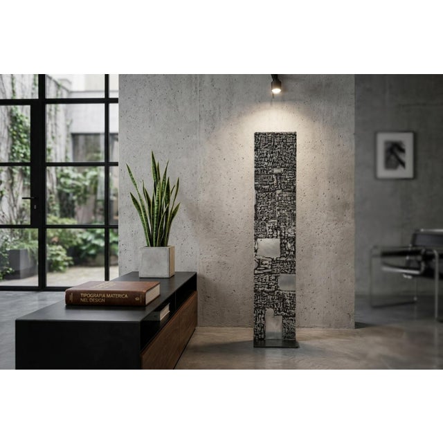 The sculpture is a cast aluminum metal stele whose surface is decorated with a relief of letters and numbers. width 23 cm...