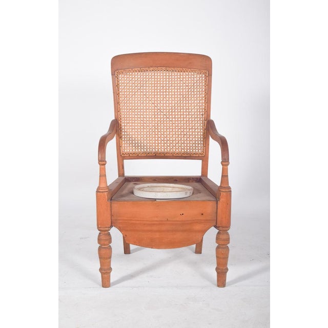 Potty chair with straw back. In light wood, with a hollowed-out seat and a central opening where a crockery container...