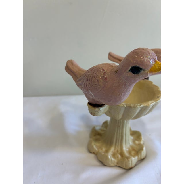 A delightful vintage cast iron bird feeder featuring two hand-painted pink birds perched on either side of a scalloped...