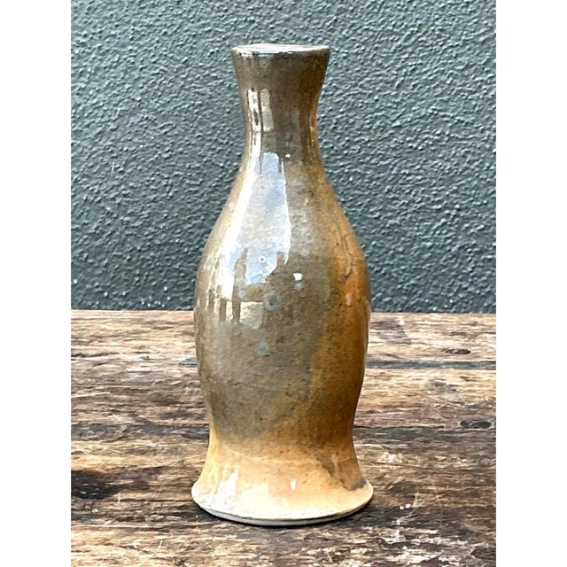 This vintage stoneware vase presents a slender, elegant silhouette, its form swelling gently at the shoulder before...