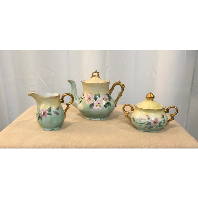 A 3-piece set including a coffee/tea pot, sugar bowl and milk dispenser all beautifully hand painted with pink flowers and...