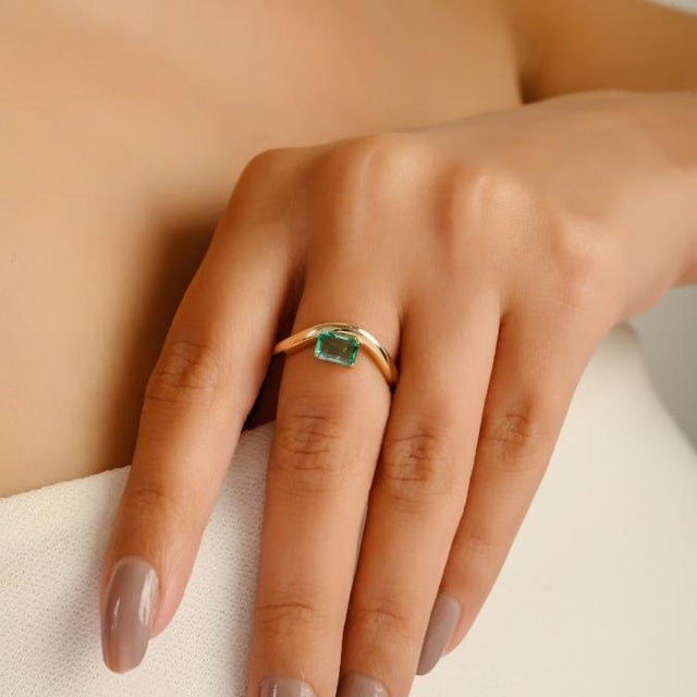 This elegant solitaire wave ring showcases a 1 carat octagon-cut natural emerald, weighing 0.54 carats, set in rich 14K...