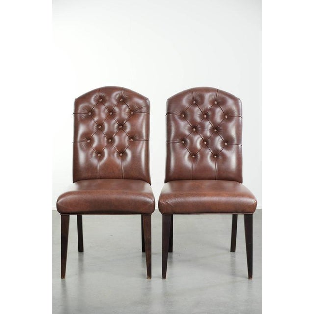 This set of 6 elegant cognac-colored cowhide leather Chesterfield dining chairs is in the English style. A dining chair is...