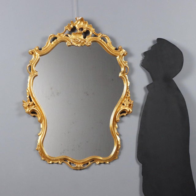 Barocchetto style mirror crafted in carved and gilded wood, featuring a molded frame with refined floral carvings and...
