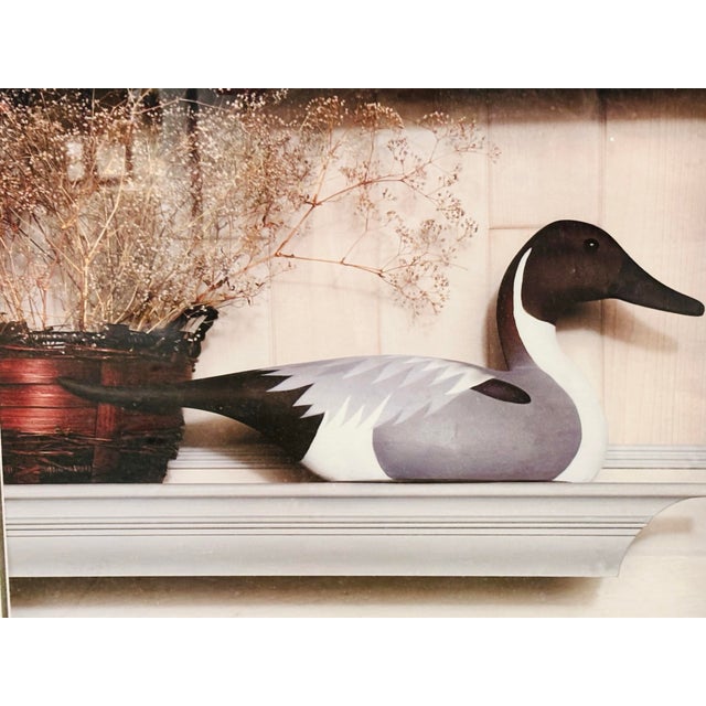 Charming framed print featuring a decorative duck decoy displayed on a mantel alongside dried florals. Presented in a...