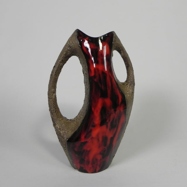 A unique vintage Fat Lava-style vase, crafted in warm red tones with a rough lava texture and openwork handles. The front...