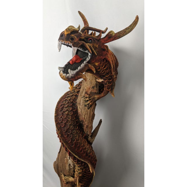A commanding monumental hand-carved Asian dragon sculpture dramatically entwined around a naturally weathered tree trunk,...