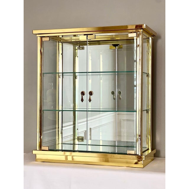 Striking Mastercraft style brass and glass mirrored table/countertop showcase vitrine cabinet. It features a tempered...