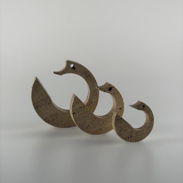 Executed in solid roman travertine, the three abstract creatures evoke stylized serpents or mythological dragons through a...