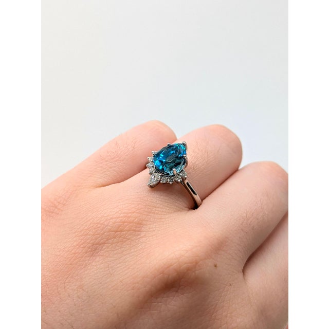A pear-shaped 9x7mm Blue Zircon takes center stage in this romantic 4.75 carat ring, surrounded by natural diamond...