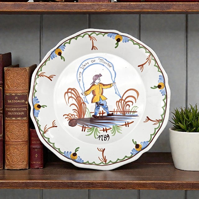 This French faïence plate presents a hand-painted folkloric figure rendered in the traditional Provençal manner associated...