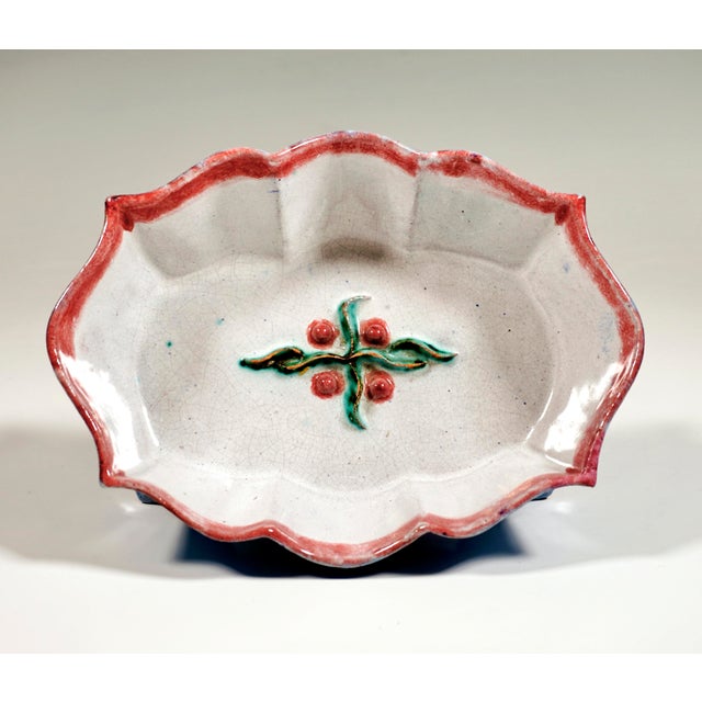 Bowl on an oval ground plan with flared, wavy and curved walls on four swept-out feet, fruit and leaf decoration in relief...