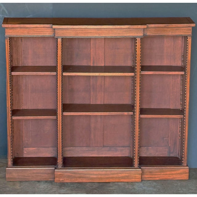 A fine English breakfront open bookcase of mahogany from the Edwardian era, featuring a frieze of three sections, with...