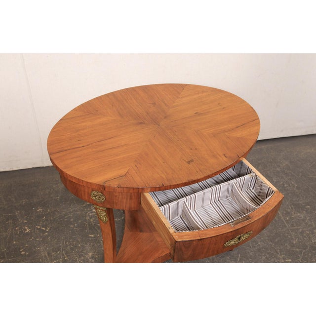A French Empire style oval side table, with brass accents, from the turn of the 19th and 20th century. This antique table...