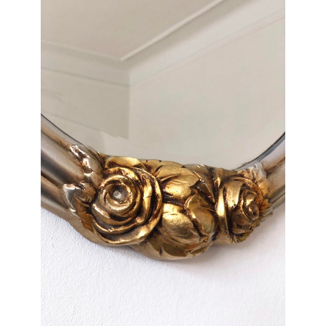 Oval silver beveled mirror with golden rose accents, inspired by Rococo style and made in Italy around 1960. Object:...
