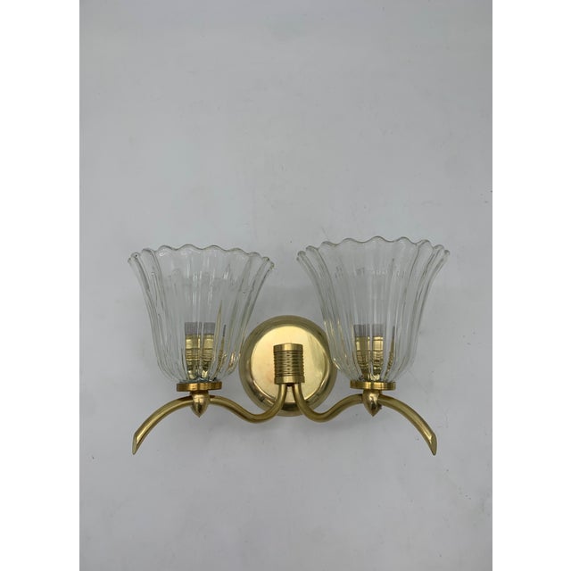 A classic-style two-light wall sconce featuring a polished brass frame and elegantly curved arms. It features two clear...