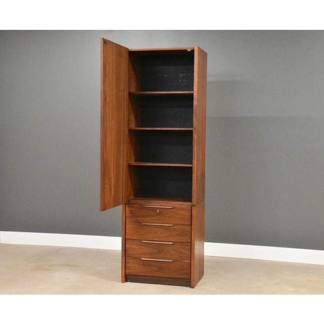 A mid century modern walnut tall dresser armoire with one large door, adjustable shelving and lower drawers made by...