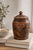 Hand-carved wooden canister with sculptural floral relief and a rich two-tone finish, offering both functional storage and...