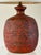 A ceramic lamp base with thick brown and red glaze. The heavy sagging drips end with small eruptions during firing....