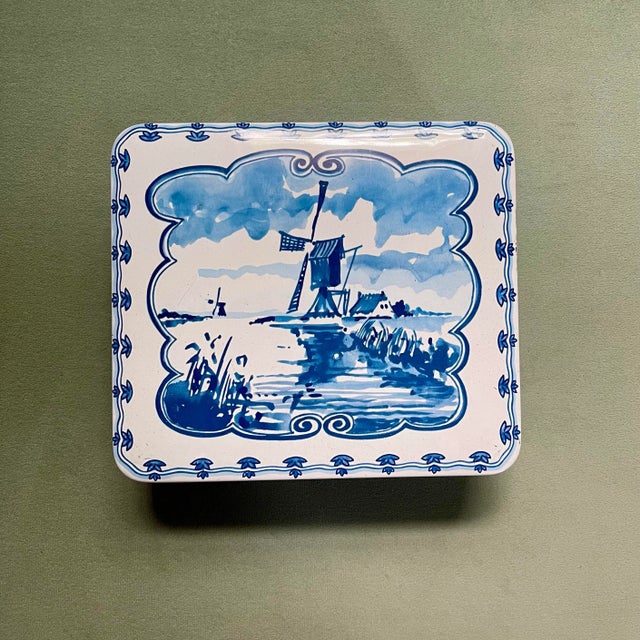 A late 20th century metal storage tin featuring a windmill scene on the lid and bordered with alternating floral & sailing...