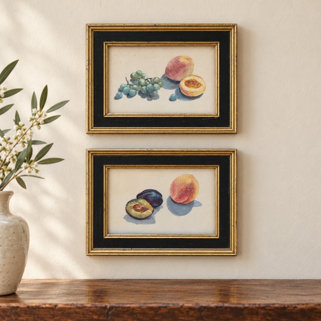 A charming pair of small framed fruit still-life artworks featuring peaches, grapes, and plums in softly muted shades of...