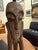 This striking wooden figure stands tall and elongated, carved with angular limbs and an expressive, mask-like face. The...